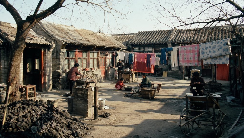 老北京大杂院场景，公用水龙头旁有人洗漱，煤堆、晾衣绳与传统房屋构成怀旧写实画面