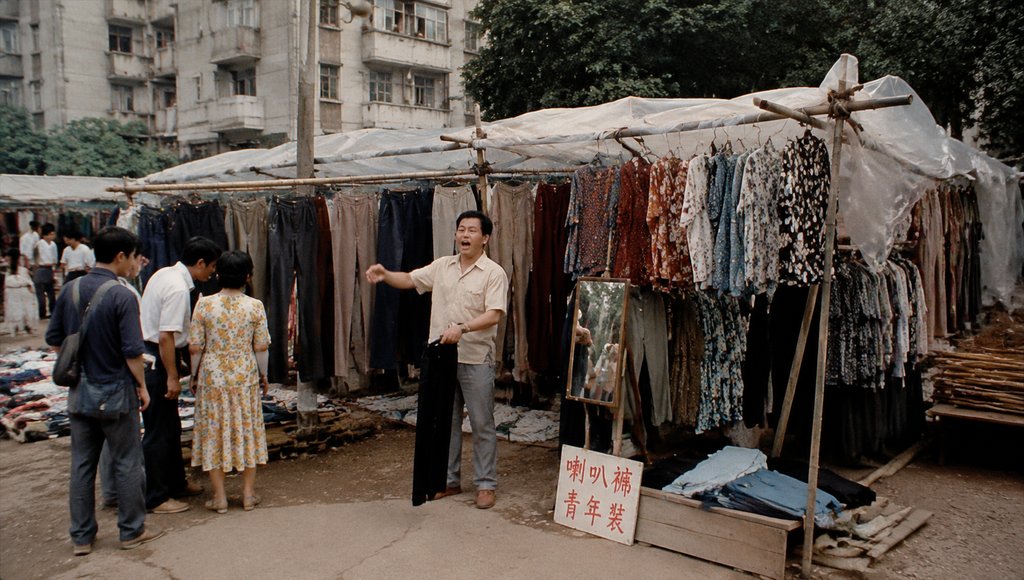 街头个体服装摊,挂满喇叭裤和青年装,塑料棚下设试衣镜,年代怀旧写实风格