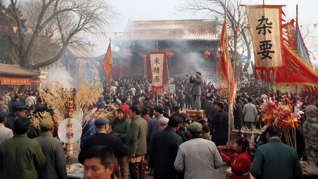 热闹的庙会场景,人群熙攘,彩旗飘扬,糖人风车和杂耍摊点缀其间,充满年代怀旧气息