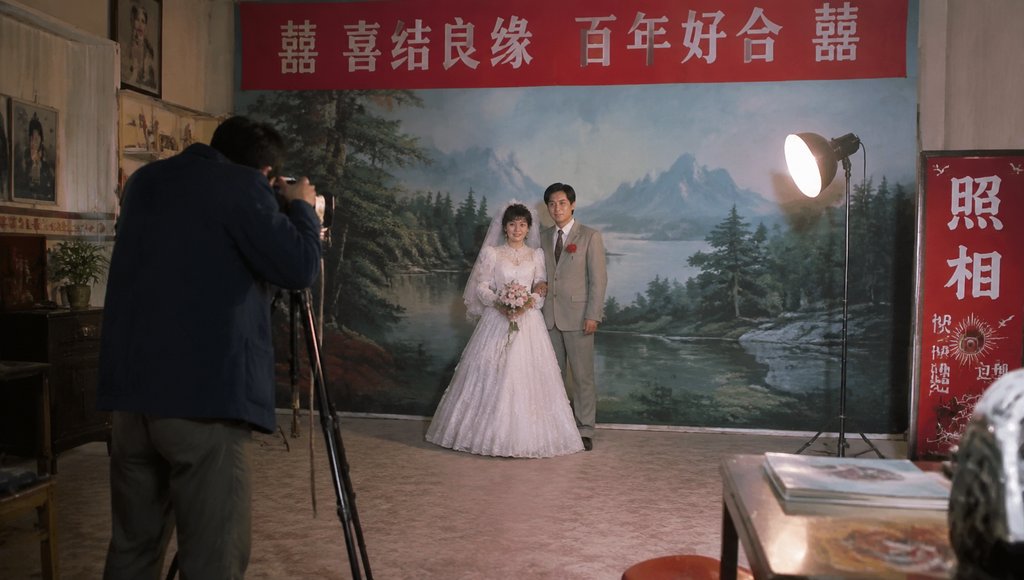 复古结婚照相馆内，新人在山水绘景前合影，摄影师拍摄，聚光灯照明，怀旧写实风格