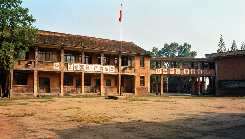 老式红砖学校建筑，连廊连接，旗杆飘扬，墙上标语醒目，怀旧写实风格