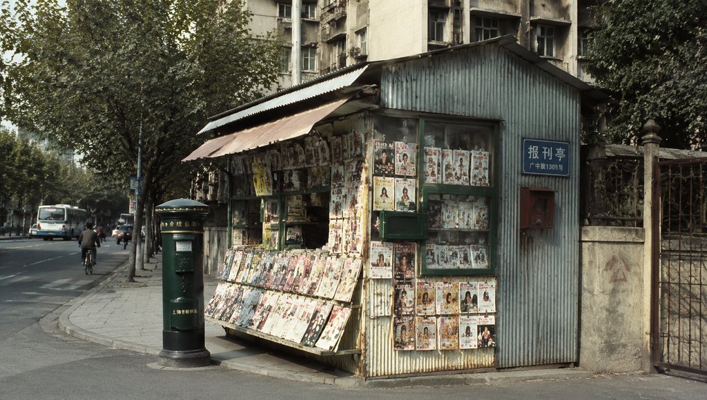 街角铁皮报刊亭，贴满旧杂志封面，旁边绿色邮筒，怀旧写实风格