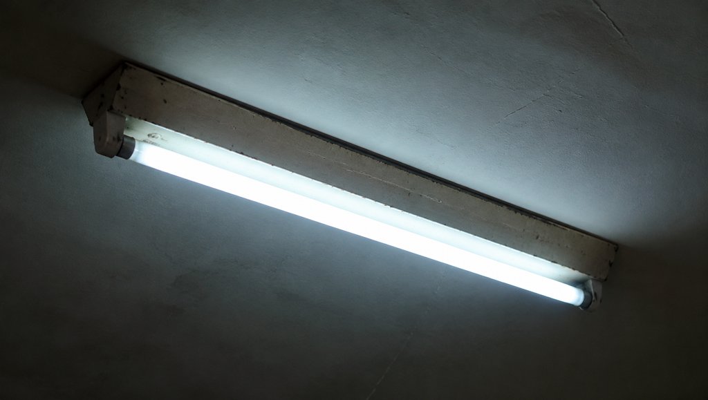 老式日光灯管发出冷白光，频闪闪烁，金属外壳老旧，怀旧写实风格