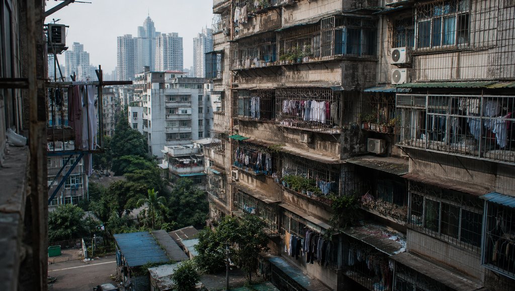 城中村老旧出租屋群,握手楼密集排列,阳台挂满衣物,背景现代高楼林立,写实都市风貌