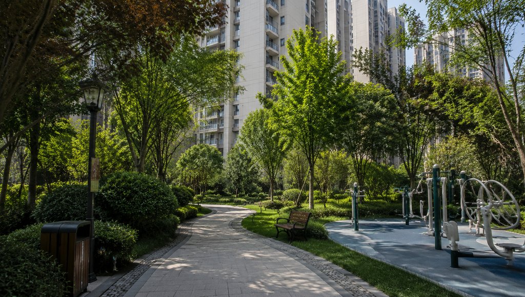 现代小区花园，绿树成荫的步道旁设有健身器材和长椅，背景为高层住宅楼，写实风格