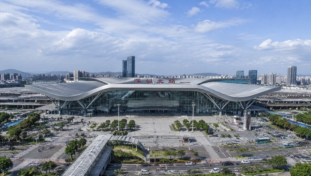 深圳北站现代高铁站建筑,流线型屋顶与玻璃幕墙设计,前方广场开阔,背景城市天际线清晰,写实风格