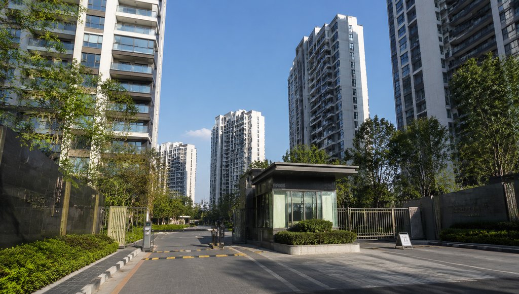 现代城市住宅小区入口，高层建筑群环绕，绿植环绕，玻璃岗亭与自动道闸，写实风格