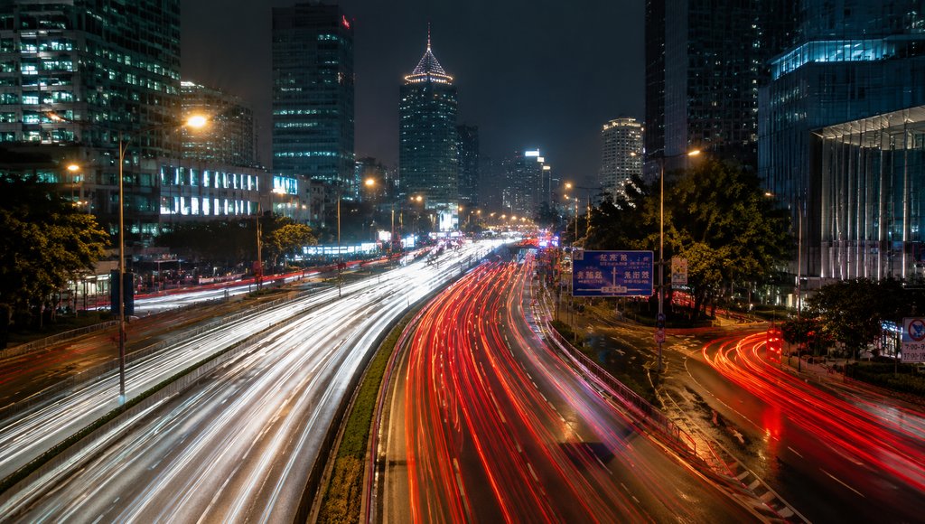 夜晚现代都市街道，车流光轨形成红白光带，高楼林立，灯光璀璨，写实风格